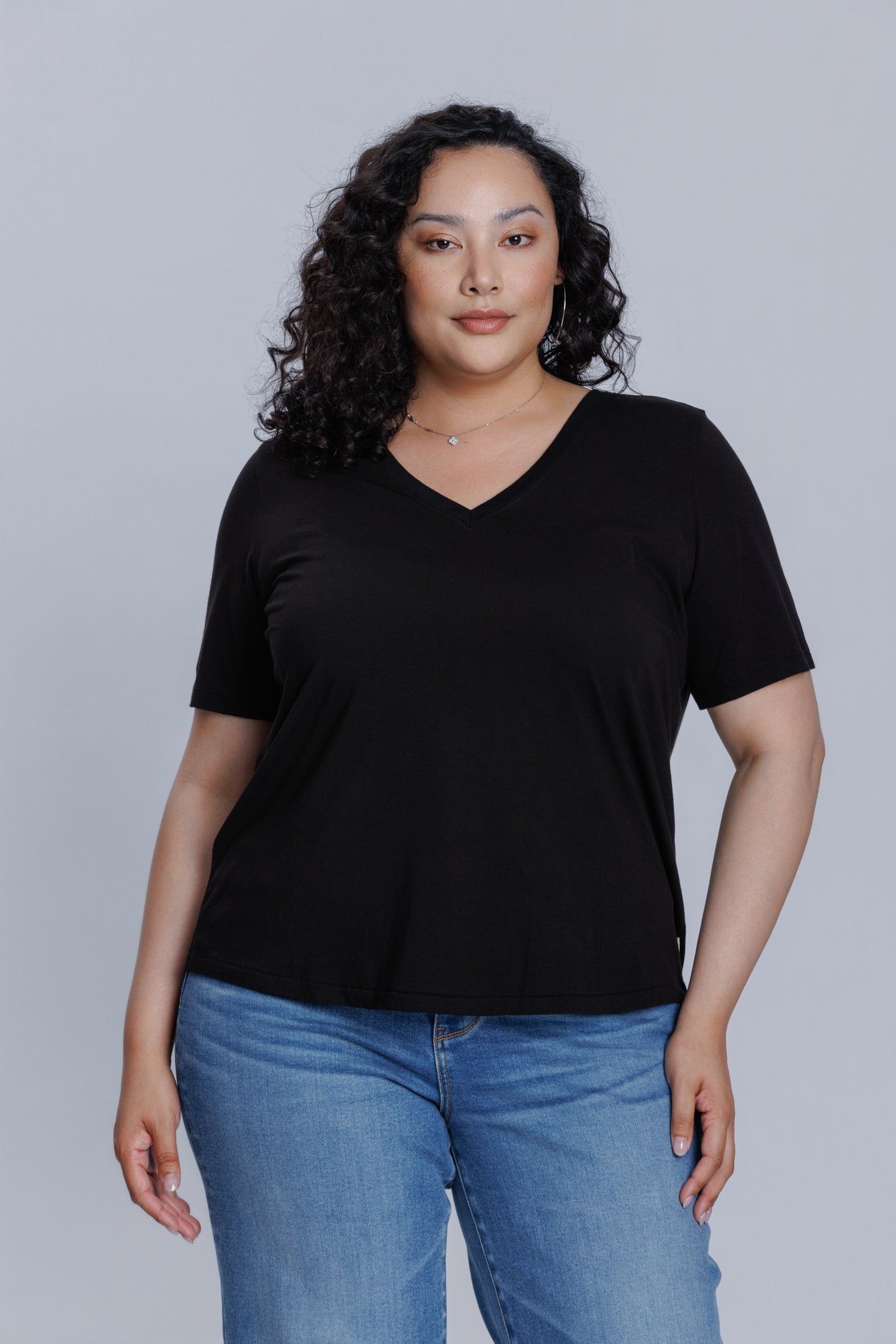 Woman wearing a DePart black t-shirt and blue skinny jeans against a light gray background | model-size: 16