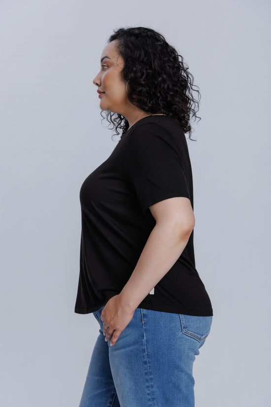 Woman wearing a DePart black t-shirt and blue skinny jeans against a light gray background