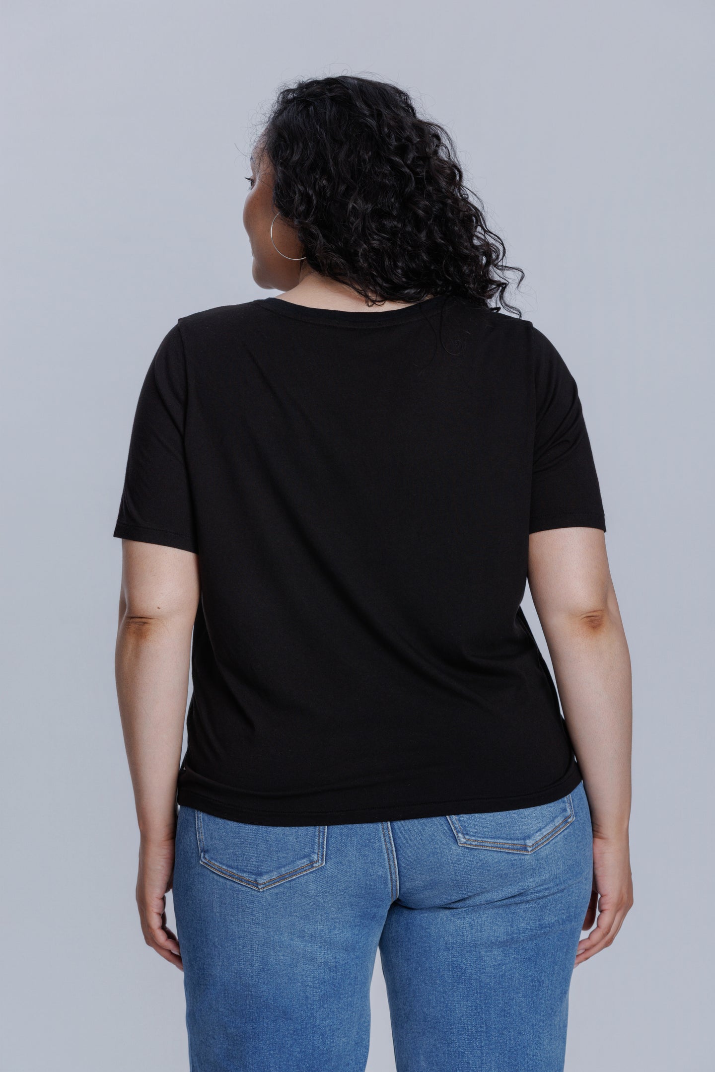 Woman wearing a DePart black t-shirt and blue skinny jeans against a light gray background