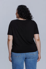 Woman wearing a DePart black t-shirt and blue skinny jeans against a light gray background