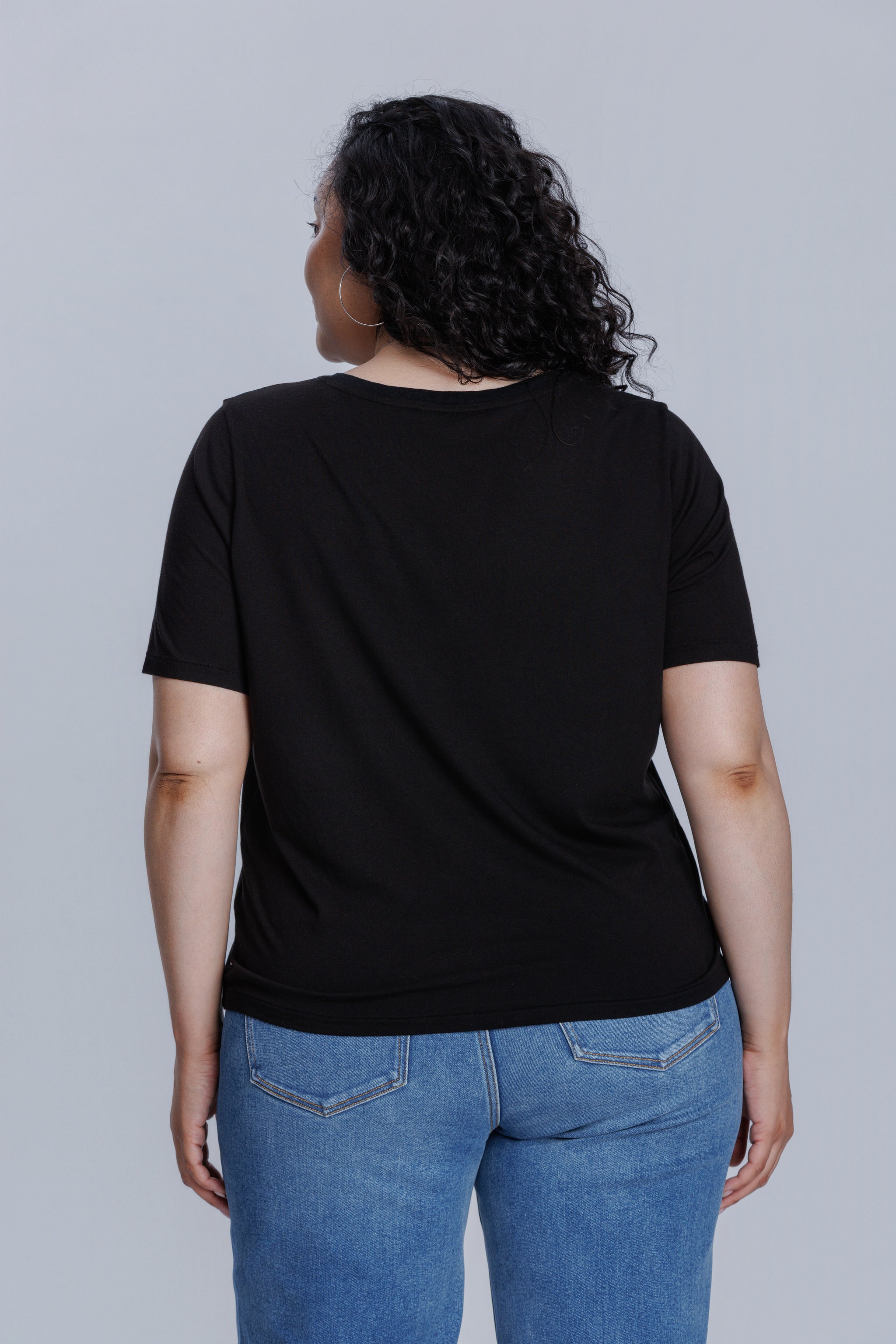 Woman wearing a DePart black t-shirt and blue skinny jeans against a light gray background