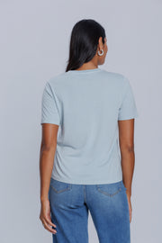 Woman wearing a DePart light blue t-shirt and blue straight jeans against a light gray background