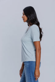 Woman wearing a DePart light blue t-shirt and blue straight jeans against a light gray background