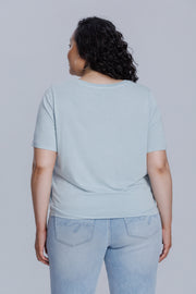 Woman wearing a DePart light blue t-shirt and light blue skinny jeans against a light gray background