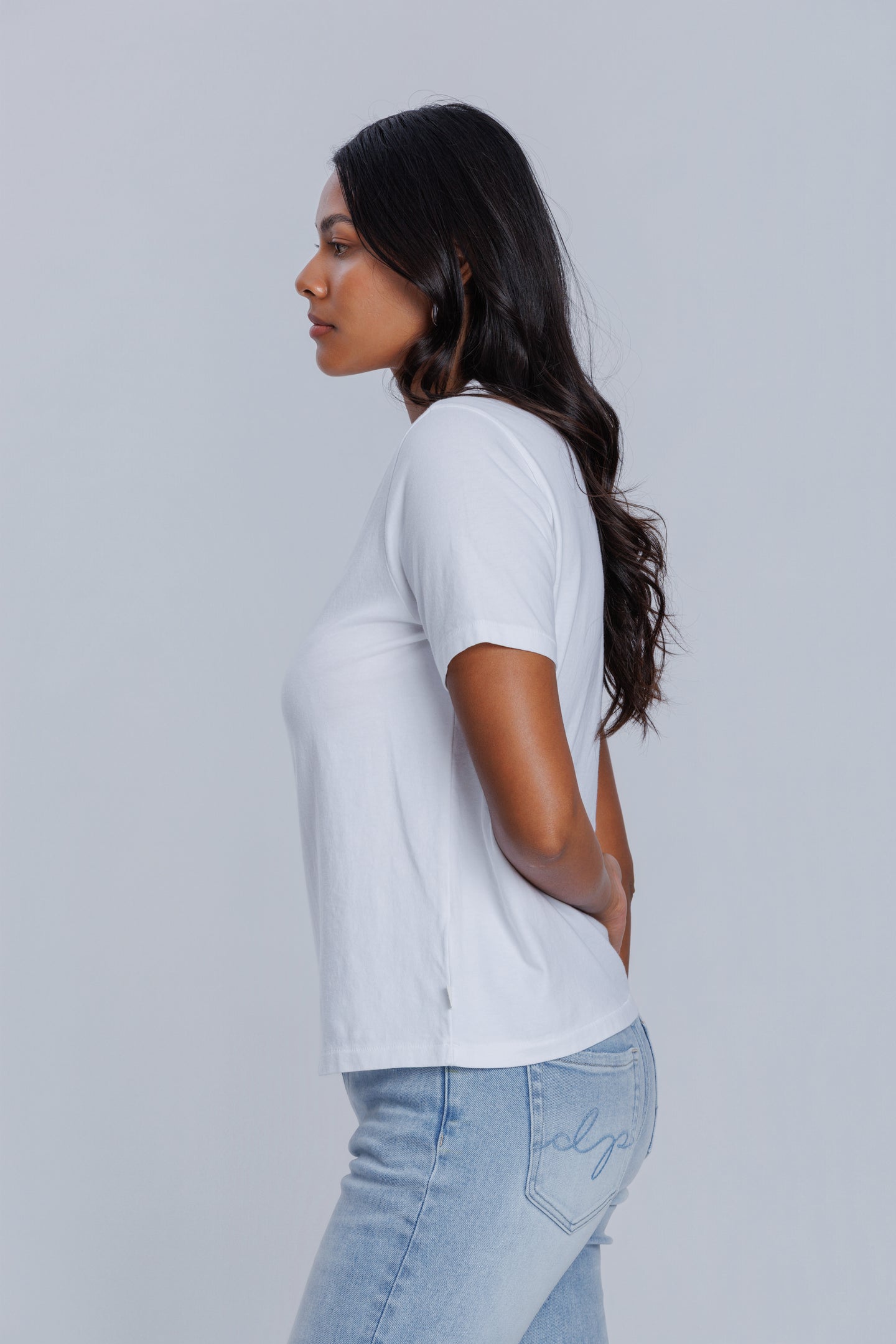 Woman wearing a DePart white t-shirt and light blue jeans against a light gray background