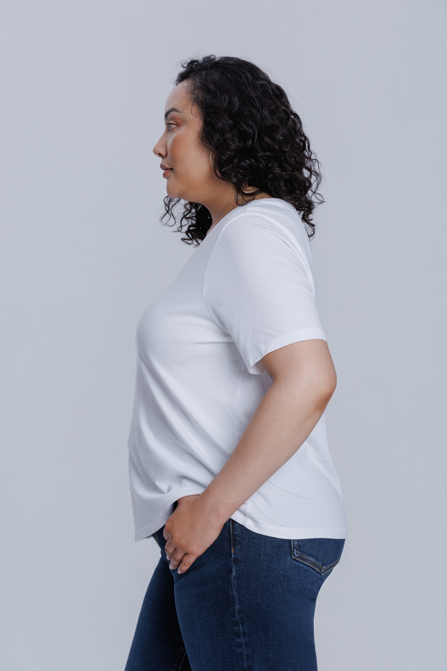 Woman wearing a DePart white t-shirt and dark blue wide leg jeans against a light gray background