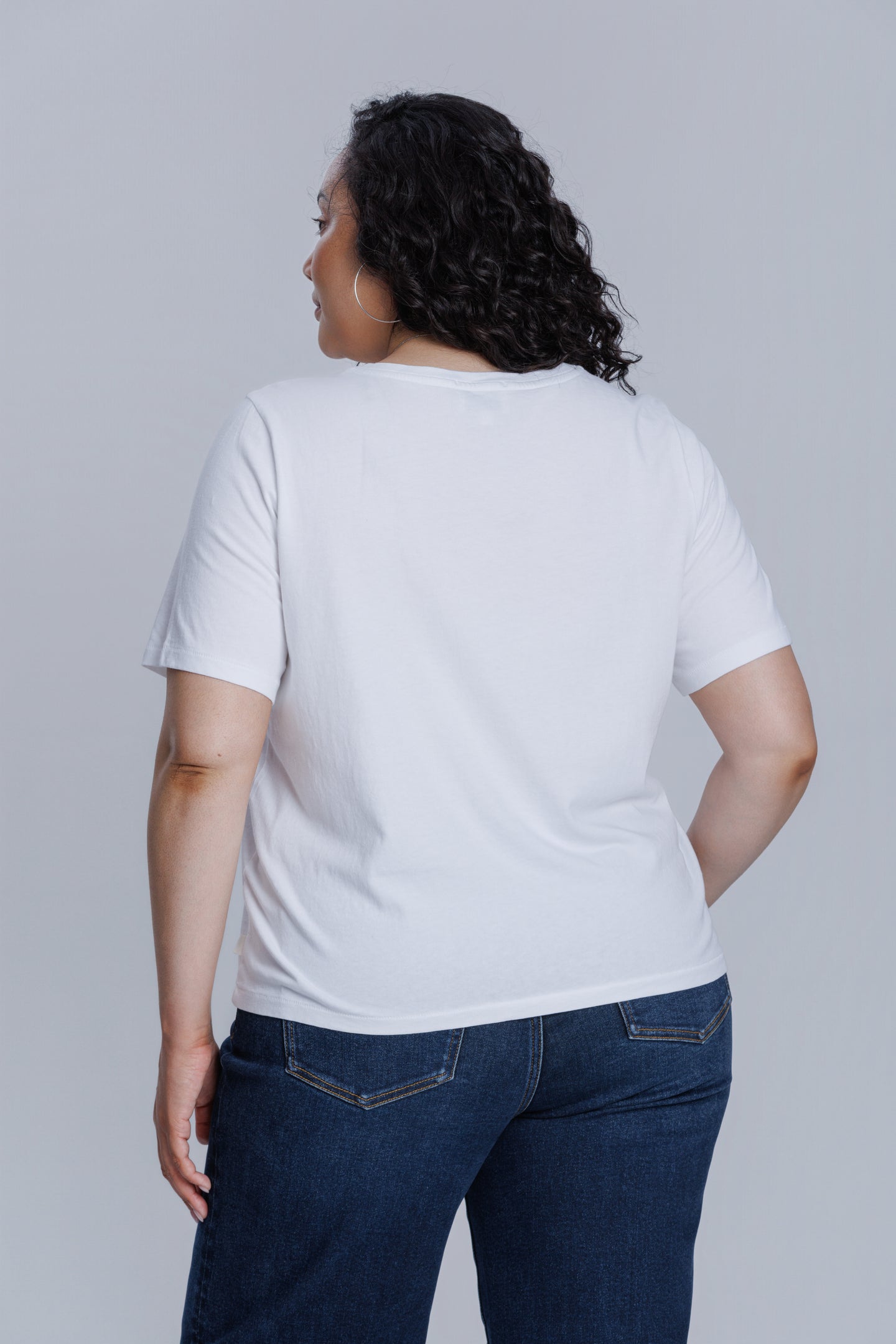 Woman wearing a DePart white t-shirt and dark blue wide leg jeans against a light gray background