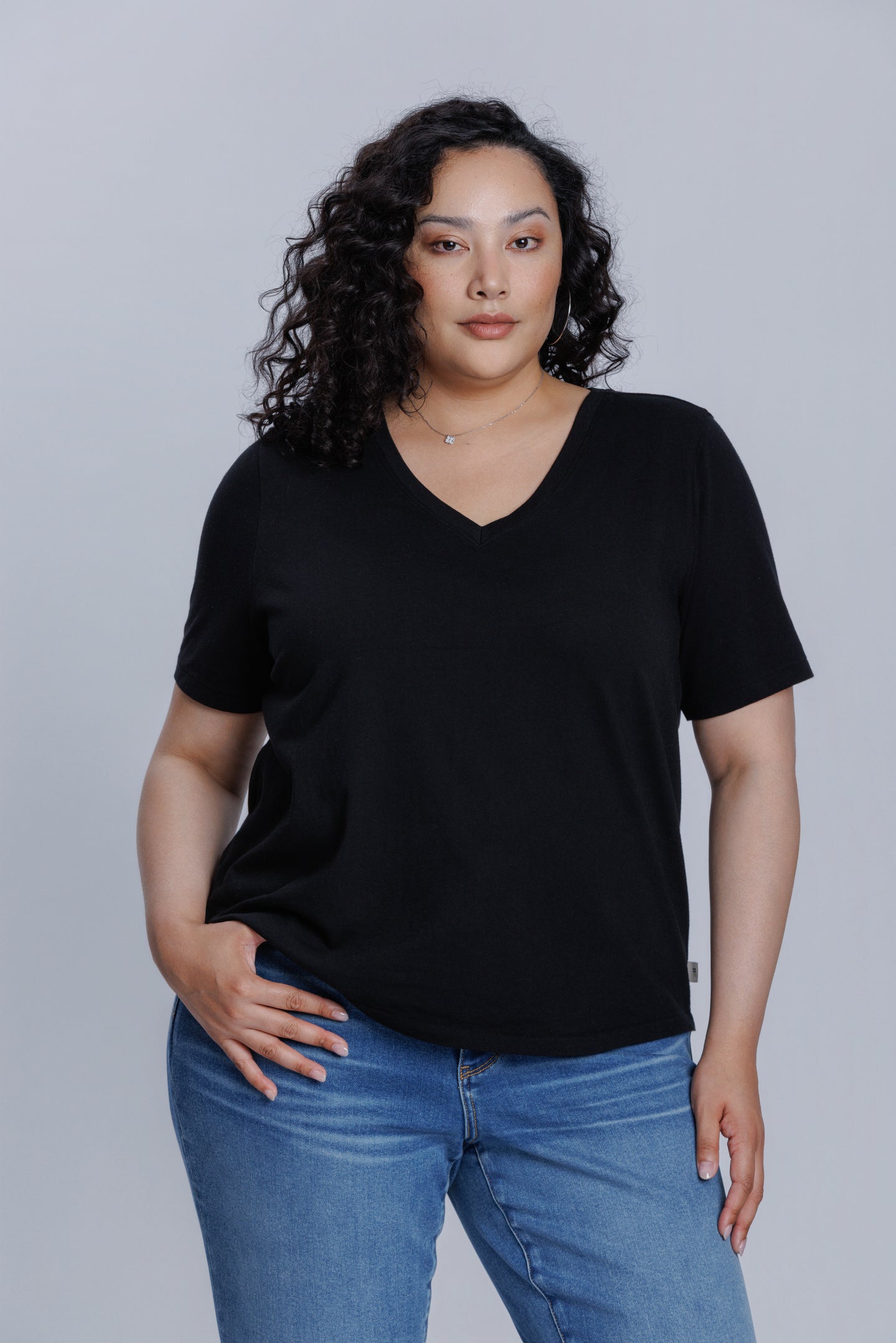 Woman wearing a DePart black t-shirt and blue straight jeans against a light gray background | model-size: 16