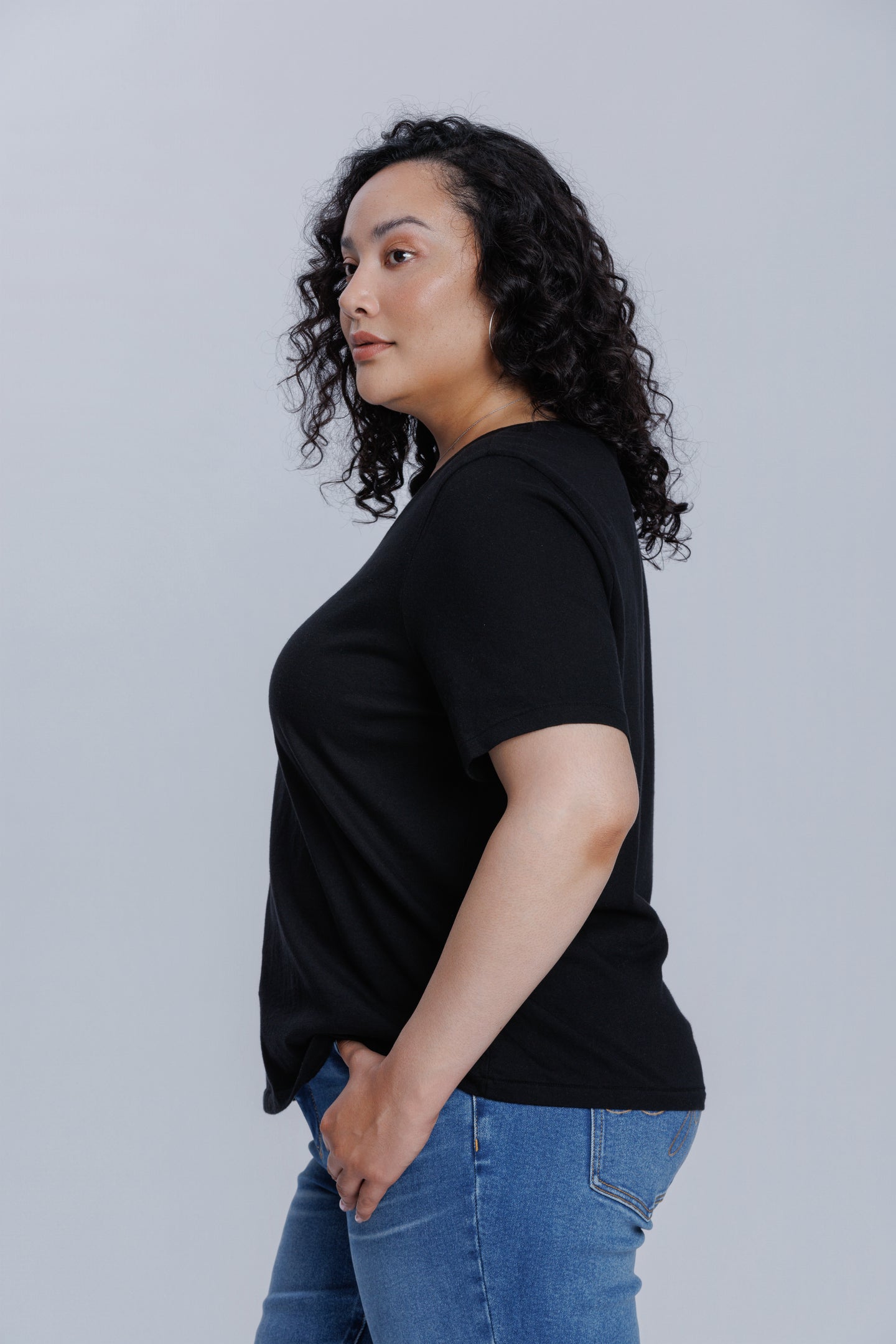 Woman wearing a DePart black t-shirt and blue straight jeans against a light gray background