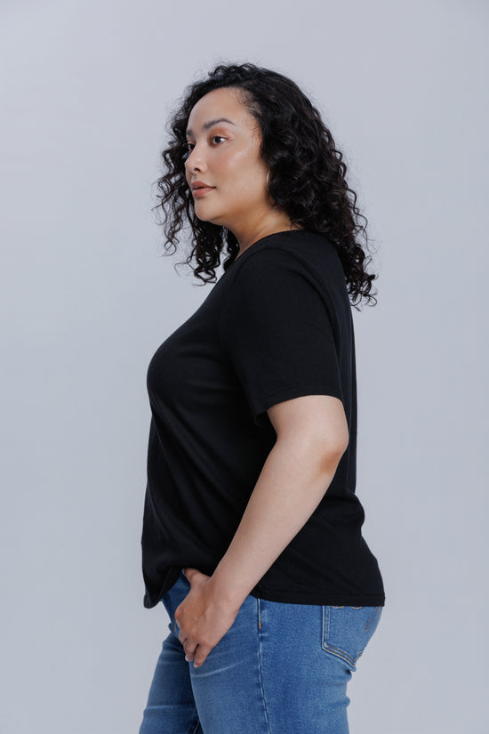 Woman wearing a DePart black t-shirt and blue straight jeans against a light gray background