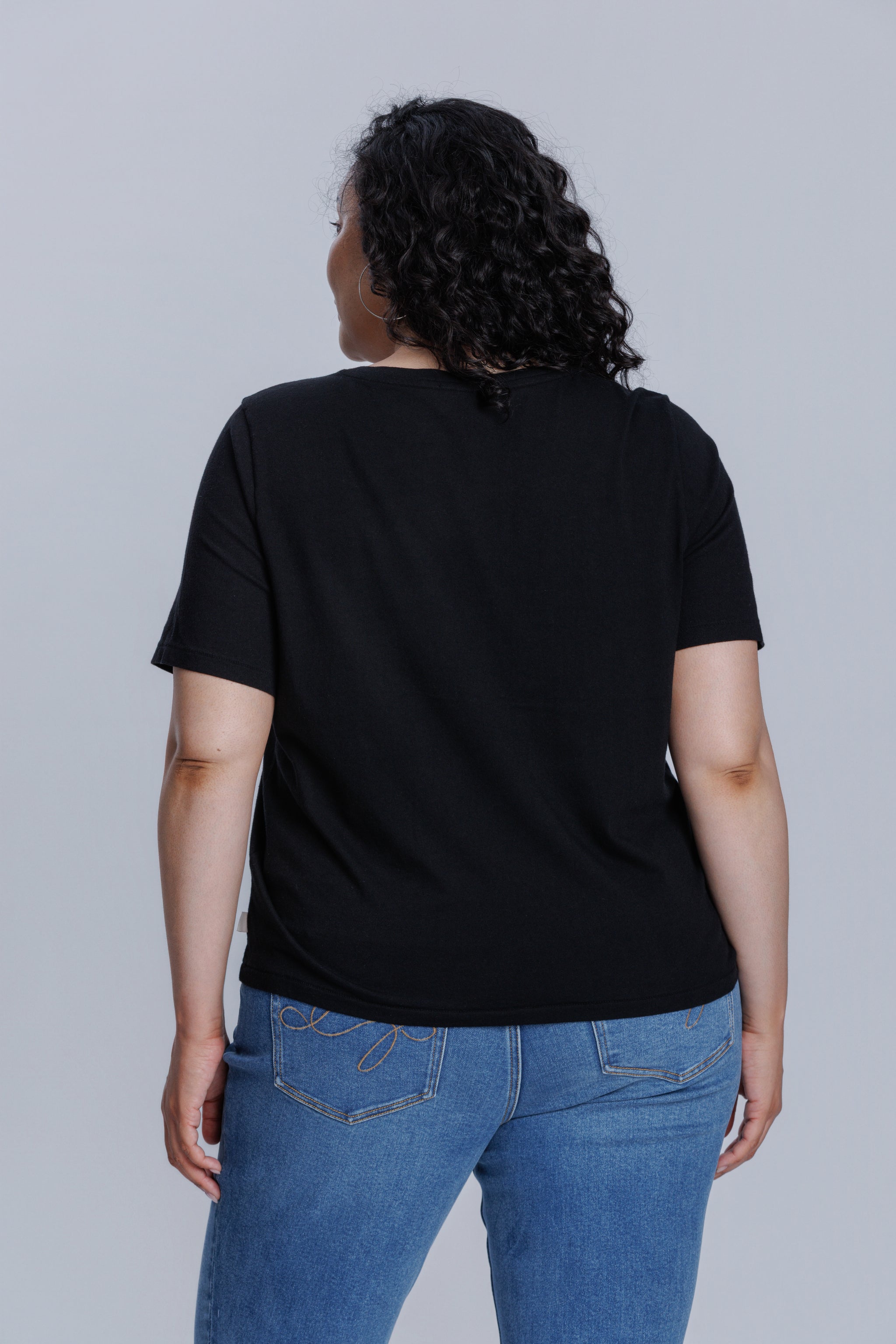 Woman wearing a DePart black t-shirt and blue straight jeans against a light gray background