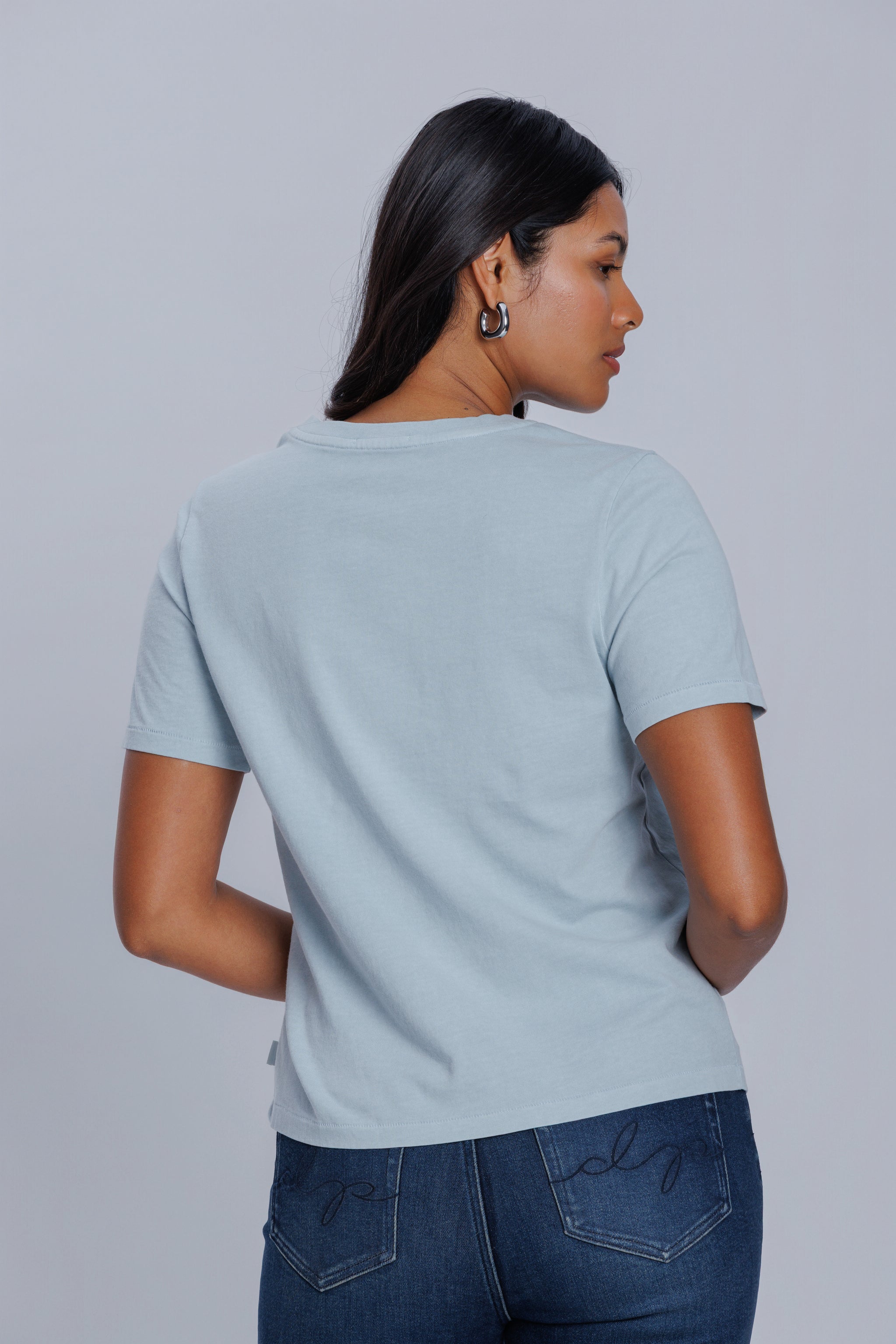 Woman wearing a DePart light blue t-shirt and dark blue straight jeans against a light gray background