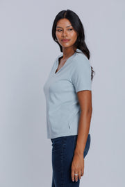Woman wearing a DePart light blue t-shirt and dark blue straight jeans against a light gray background