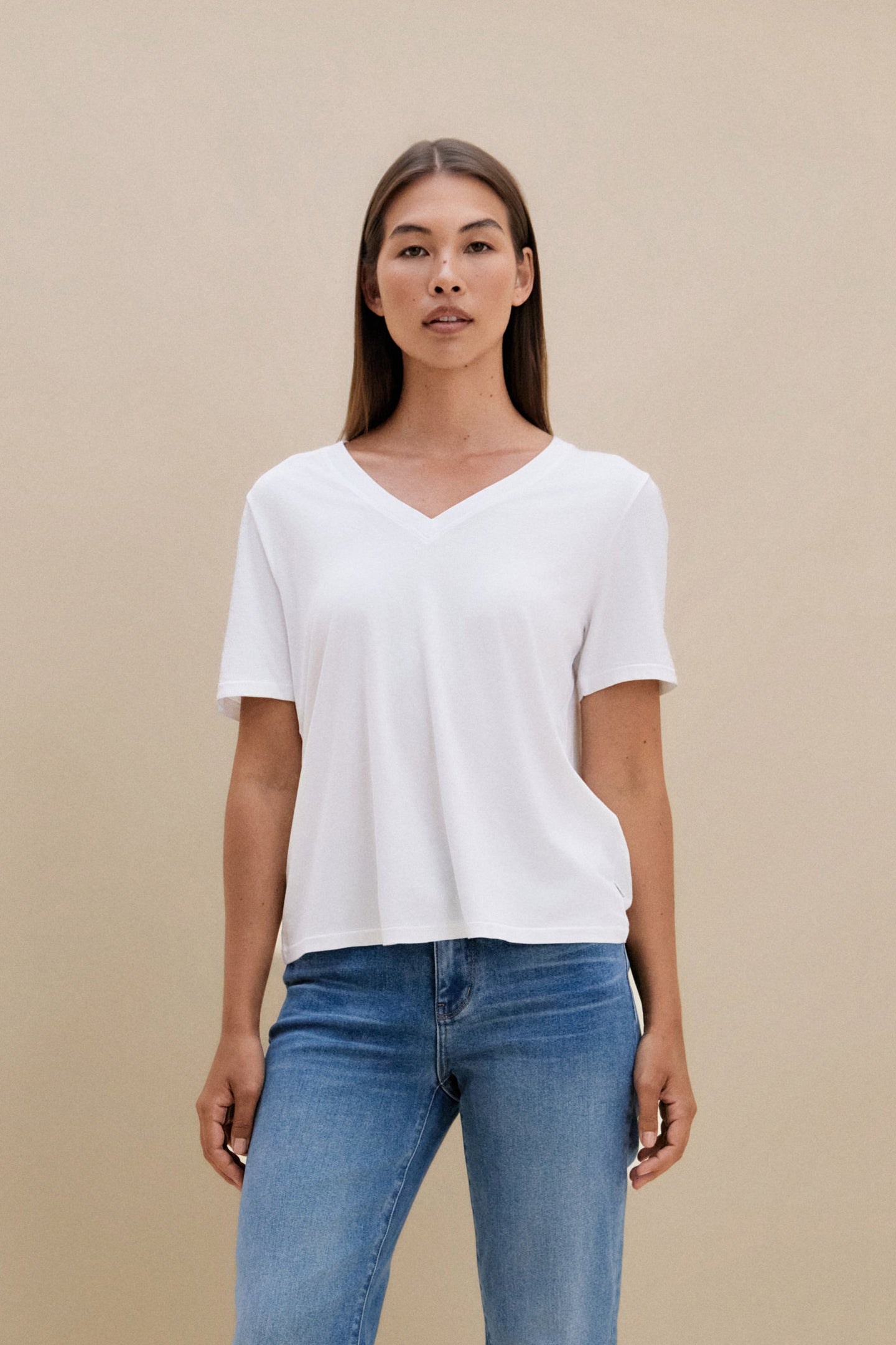 Woman wearing a white t-shirt, and blue jeans against a beige background 