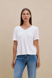 Woman wearing a white t-shirt, and blue jeans against a beige background 