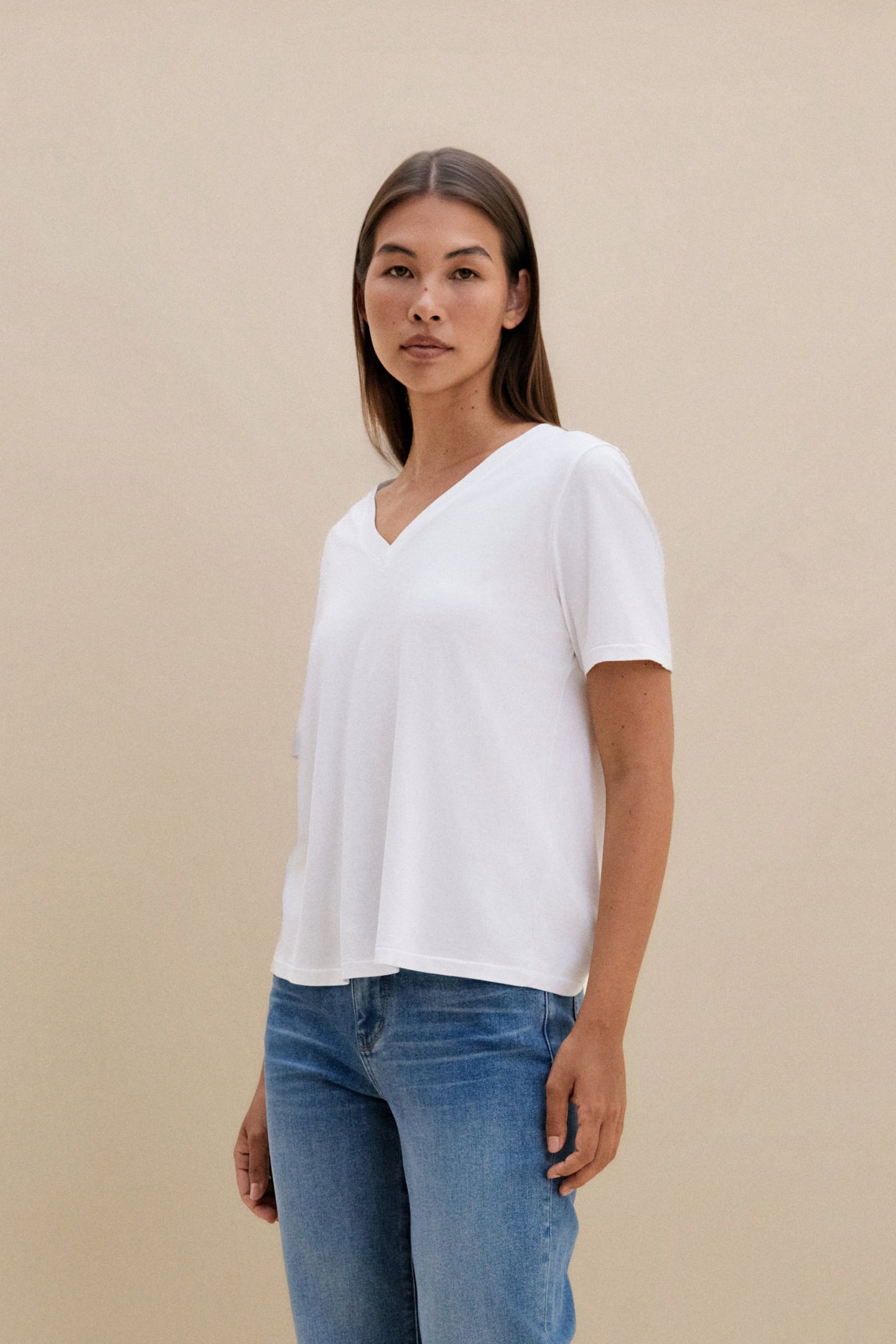 Woman wearing a white t-shirt, and blue jeans against a beige background 
