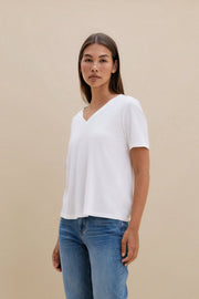 Woman wearing a white t-shirt, and blue jeans against a beige background 