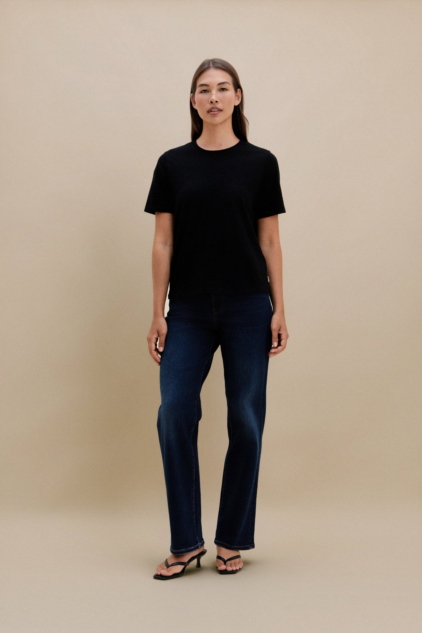 Person wearing a black t-shirt and dark jeans against a beige background