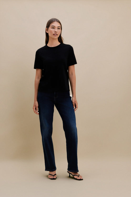 Woman wearing a black t-shirt and dark jeans against a beige background | model-size: 4