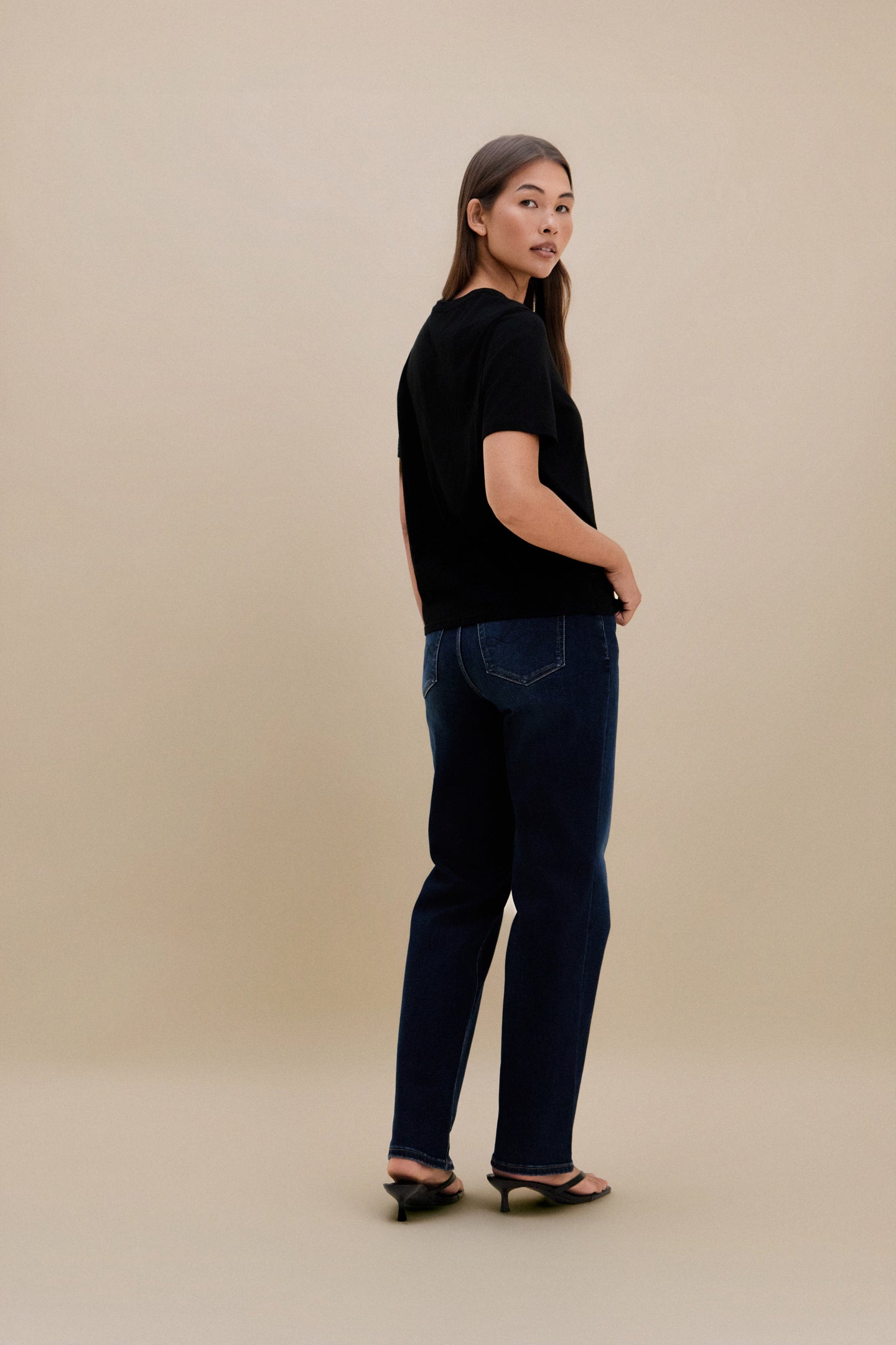 Woman wearing a black t-shirt and blue jeans against a beige background