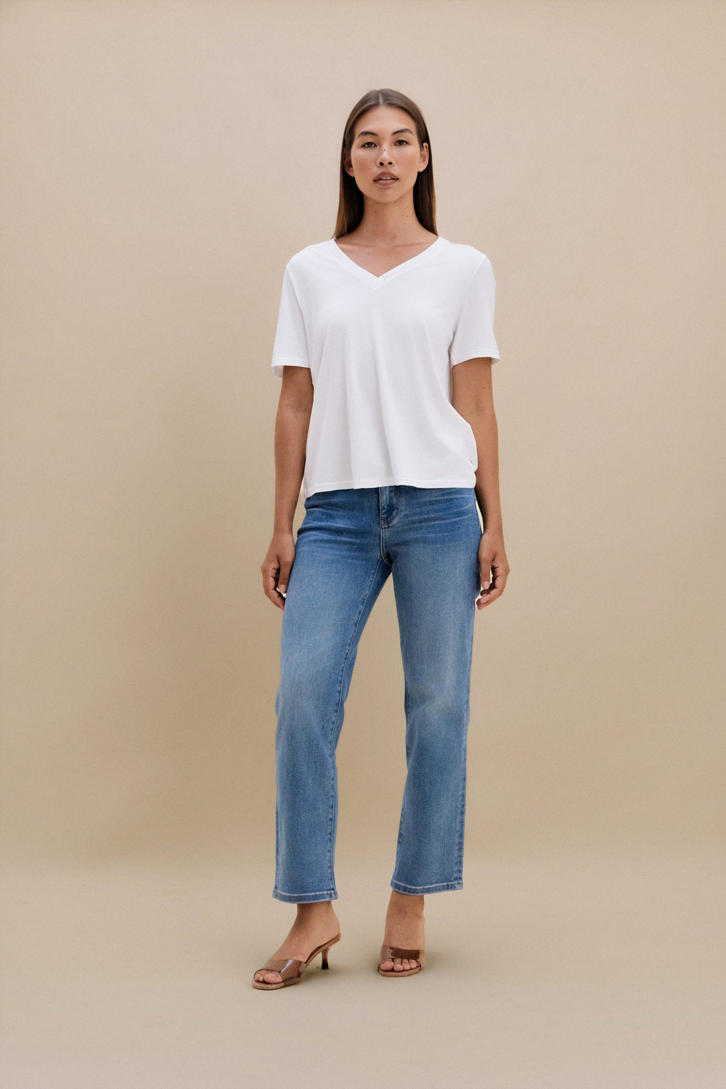 Woman wearing a white t-shirt and blue jeans against a beige background | model-size: 4