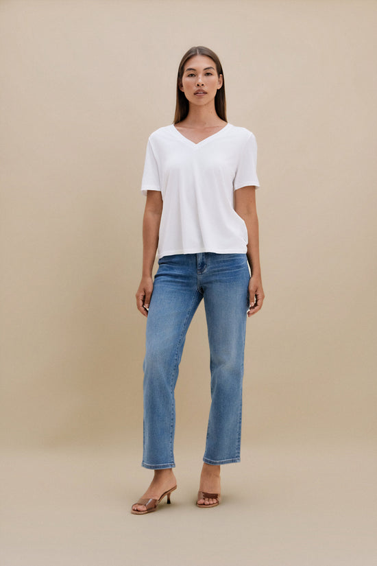 Woman wearing a white t-shirt and blue jeans against a beige background | model-size: 4