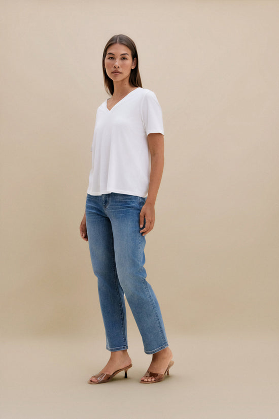 Woman wearing a white top and blue jeans against a beige background