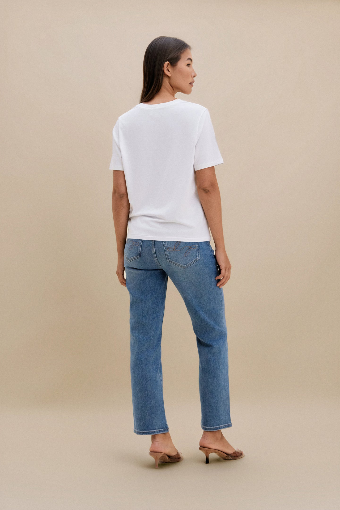 Woman wearing a white t-shirt and blue jeans on a beige background