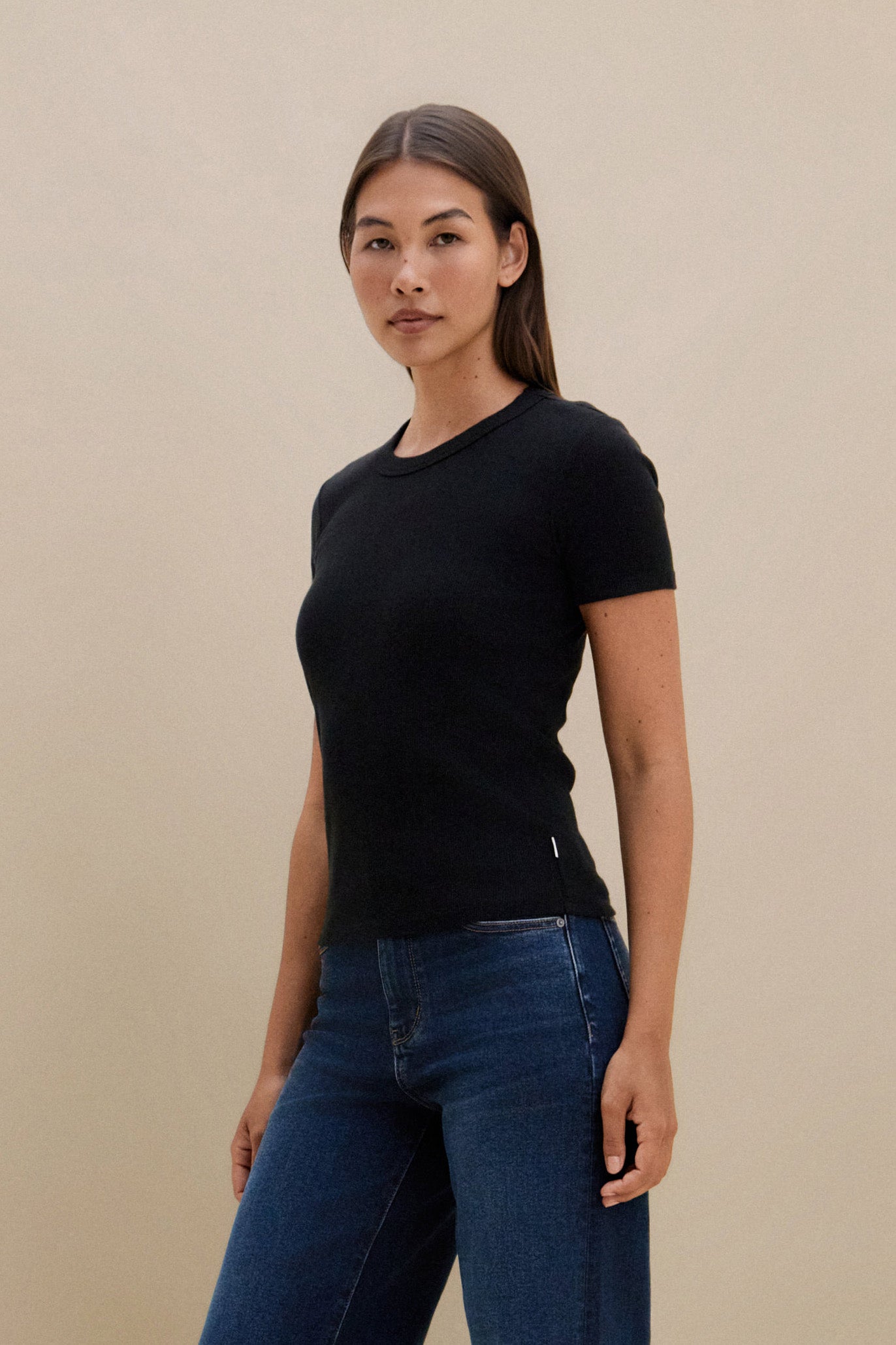 Woman wearing a black t-shirt and blue jeans against a beige background
