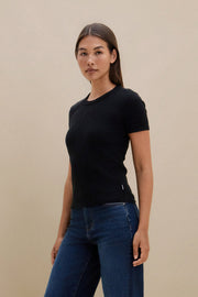 Woman wearing a black t-shirt and blue jeans against a beige background