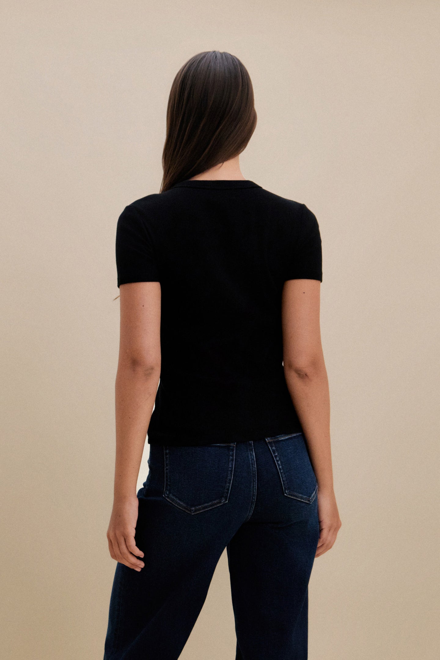 Person wearing a black t-shirt and blue jeans against a beige background