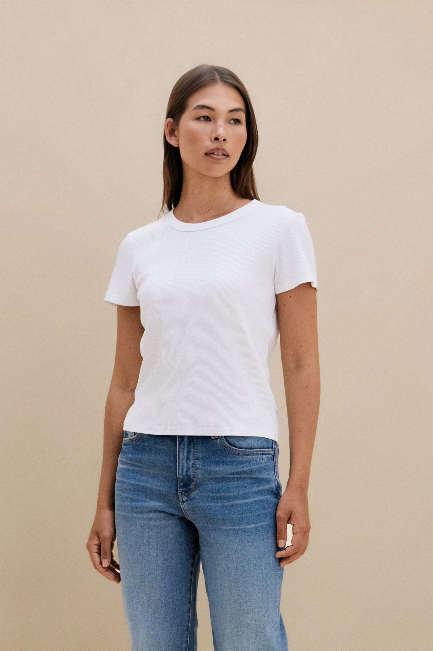 Woman wearing a white t-shirt and blue jeans against a beige background