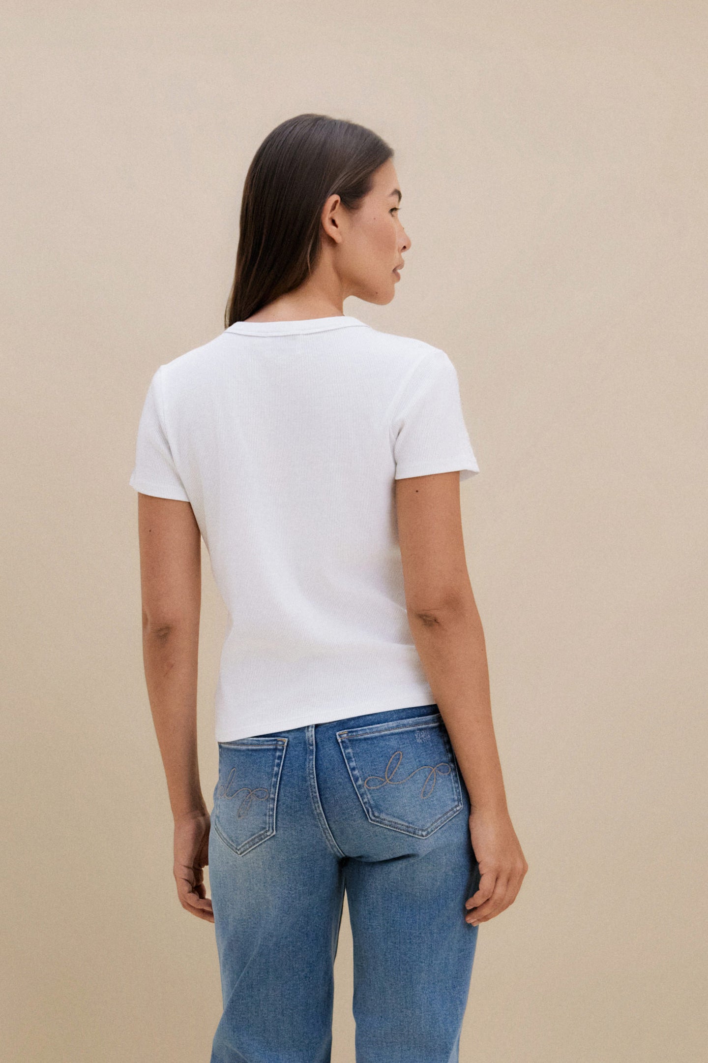 Woman wearing a white t-shirt and blue jeans against a beige background