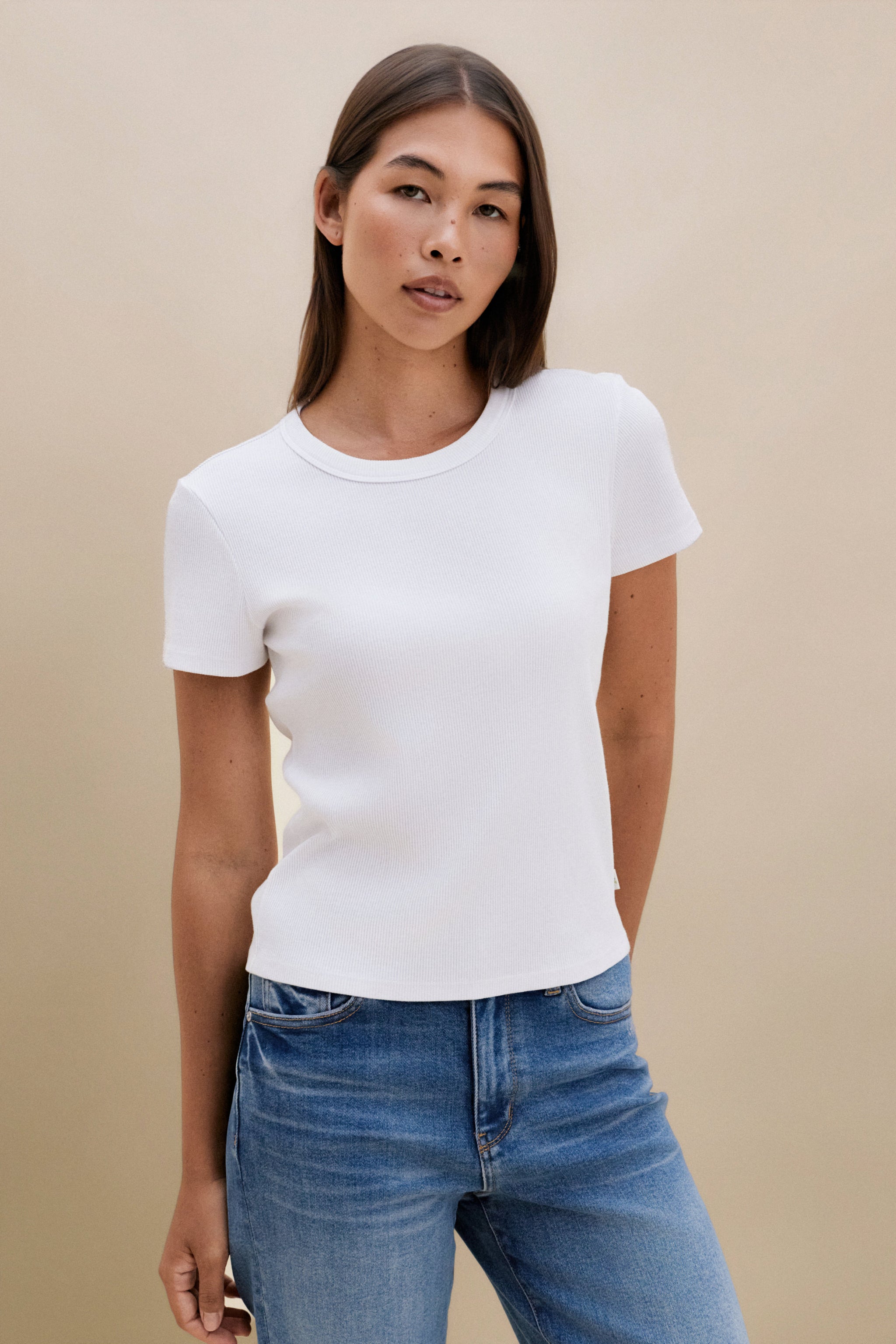 Woman wearing a white t-shirt and blue jeans against a beige background | model-size: 4