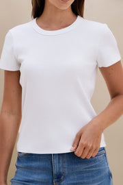 Person wearing a plain white t-shirt and blue jeans against a beige background