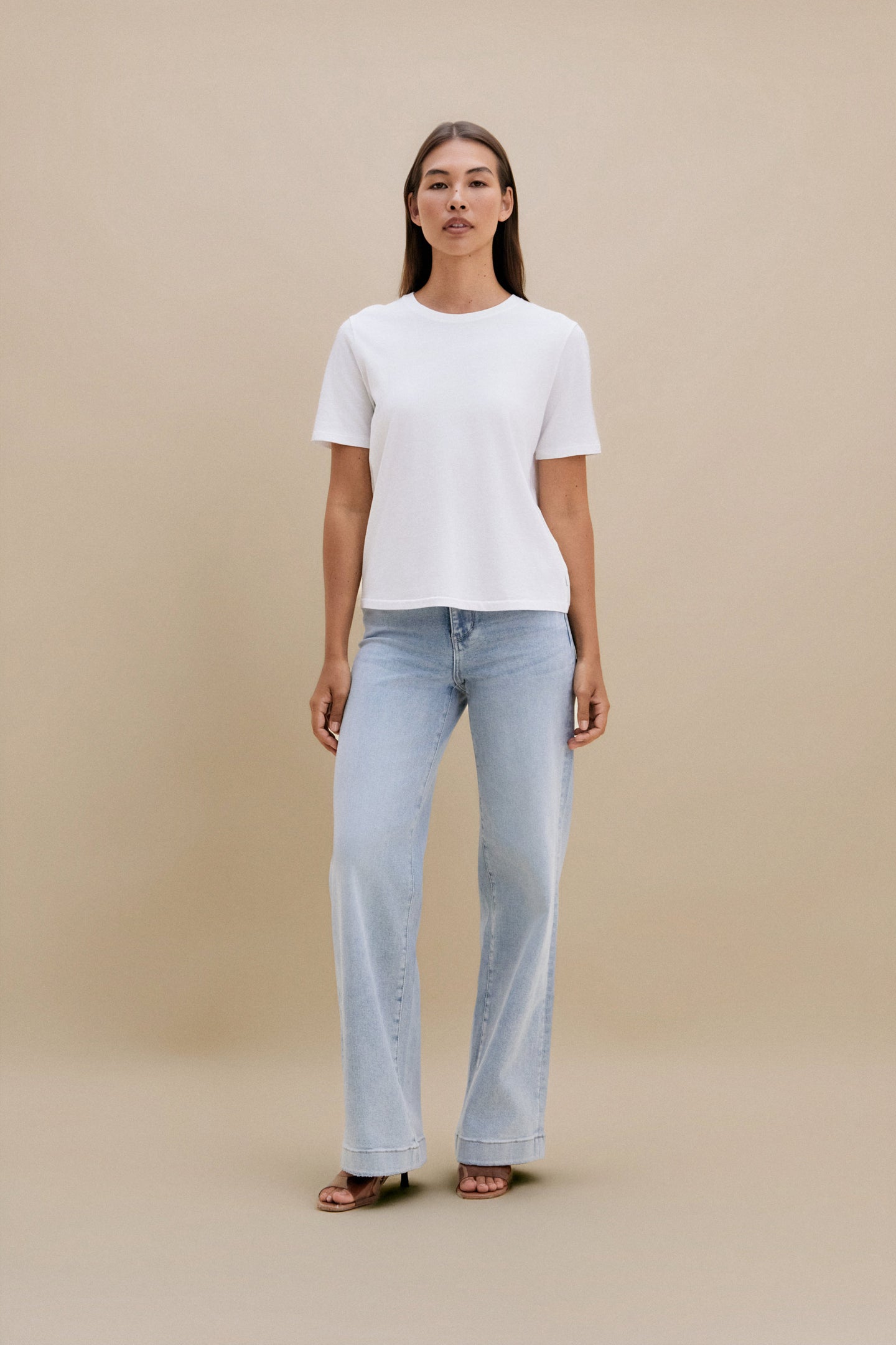Woman wearing a white t-shirt and light blue jeans against a beige background