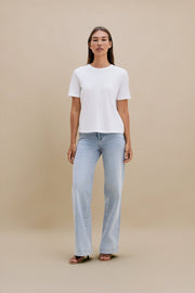 Woman wearing a white t-shirt and light blue jeans against a beige background