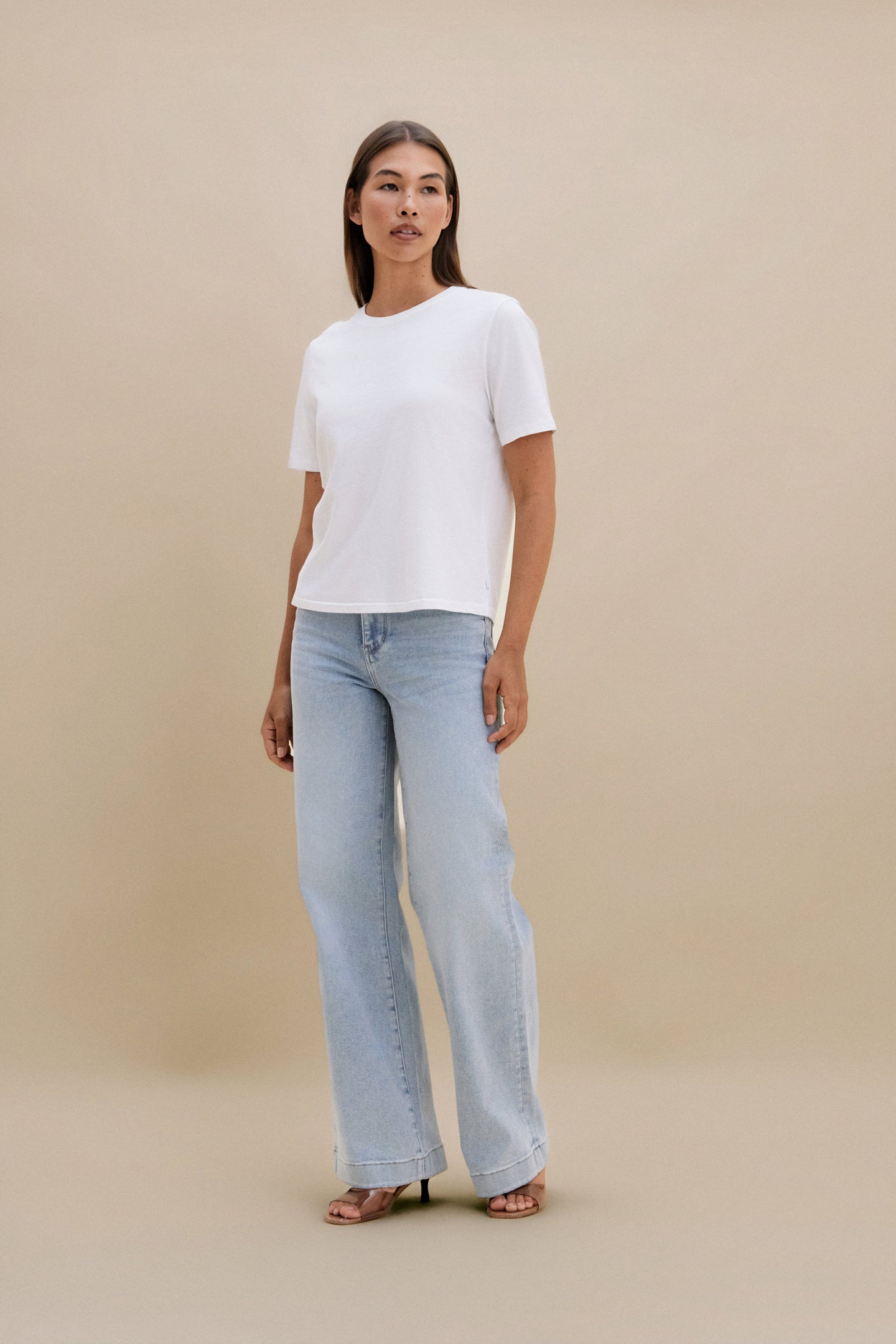 Woman wearing a white top and light blue jeans against a beige background