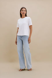 Woman wearing a white top and light blue jeans against a beige background
