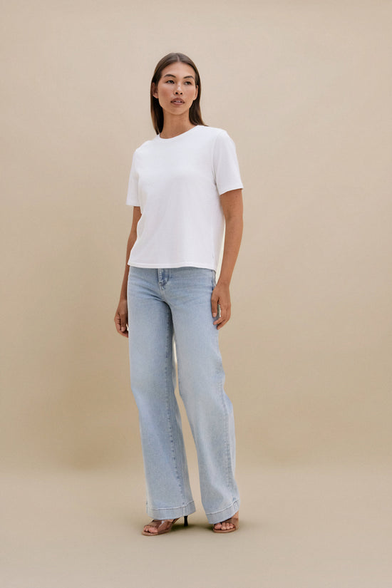 Woman wearing a white top and light blue jeans against a beige background | model-size: 4
