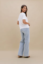 Woman wearing a white t-shirt and light blue jeans against a beige background