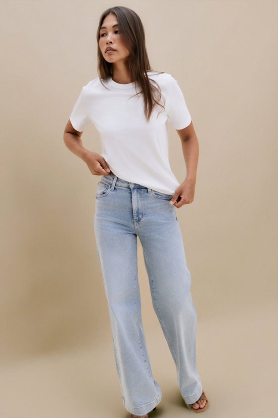 Woman wearing a white t-shirt and light blue jeans against a beige background