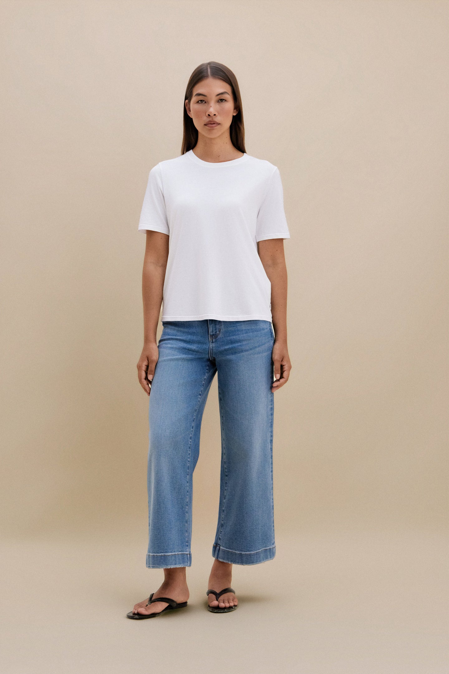 Woman wearing a white t-shirt and blue jeans on a beige background