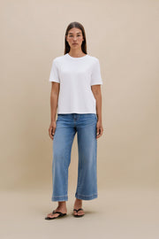Woman wearing a white t-shirt and blue jeans on a beige background