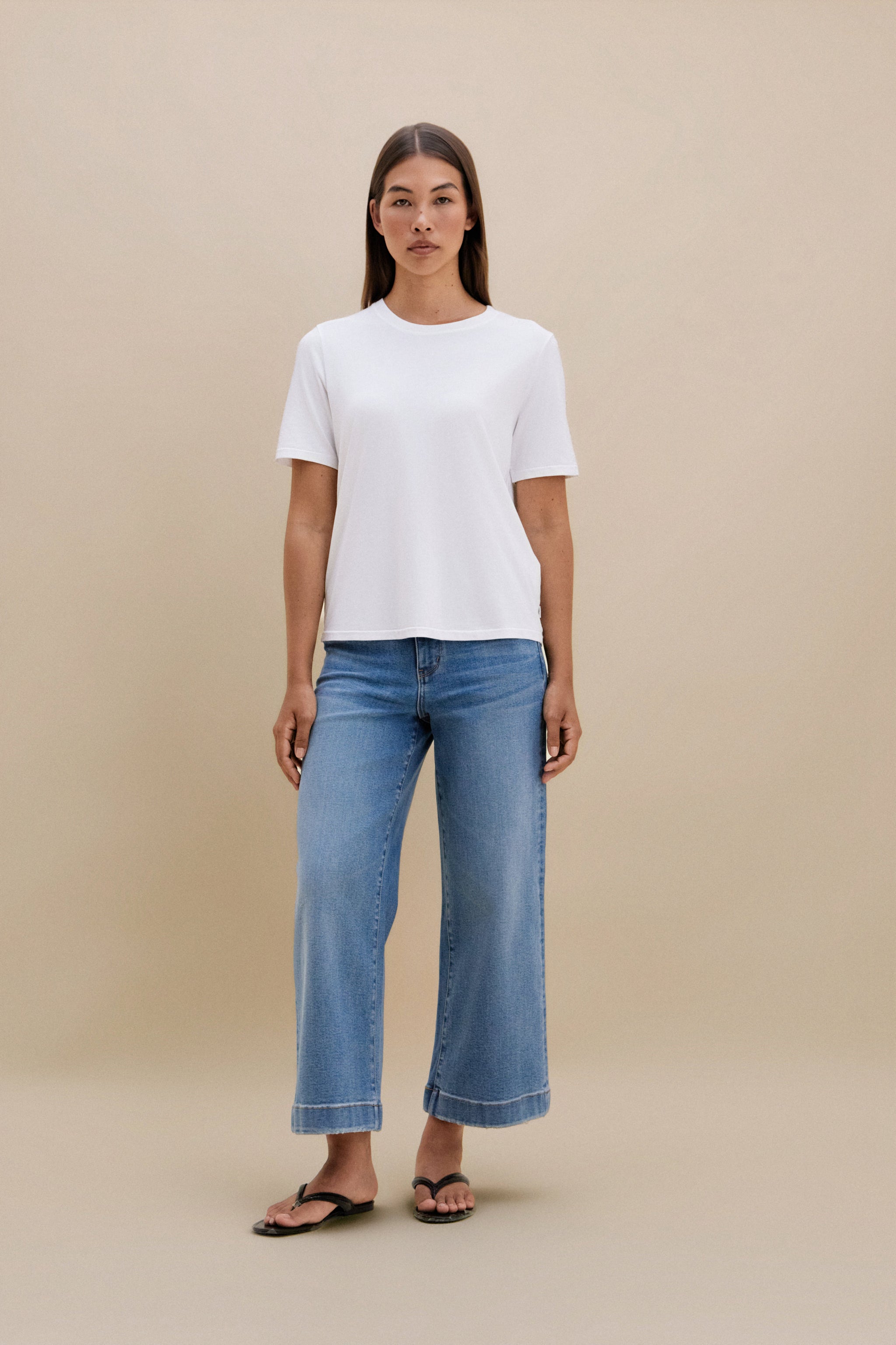 Woman wearing a white t-shirt and blue jeans on a beige background