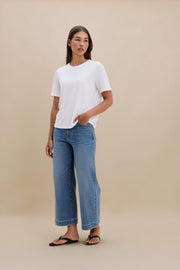 Woman wearing a white t-shirt and blue jeans against a beige background
