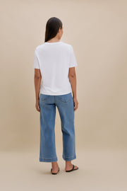 Person wearing a white t-shirt and blue jeans on a beige background