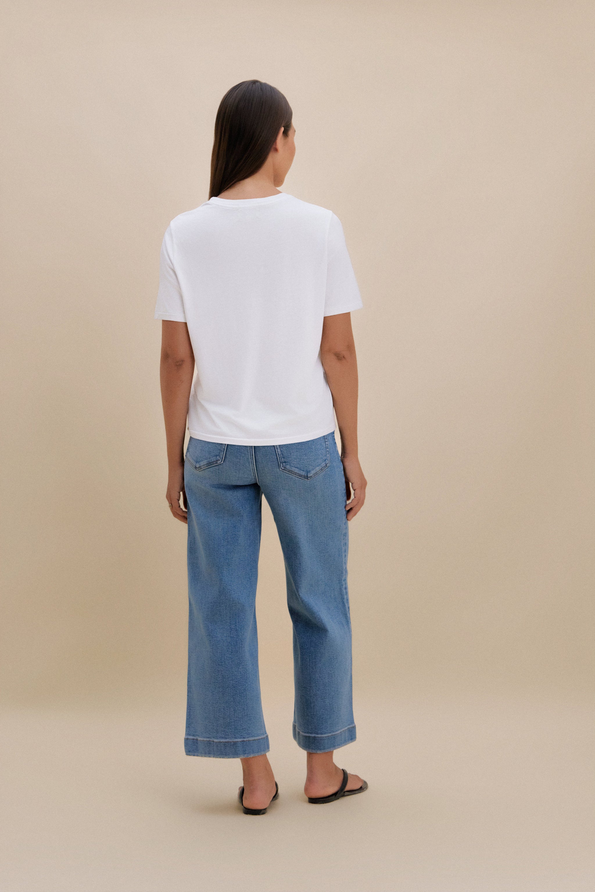 Person wearing a white t-shirt and blue jeans on a beige background