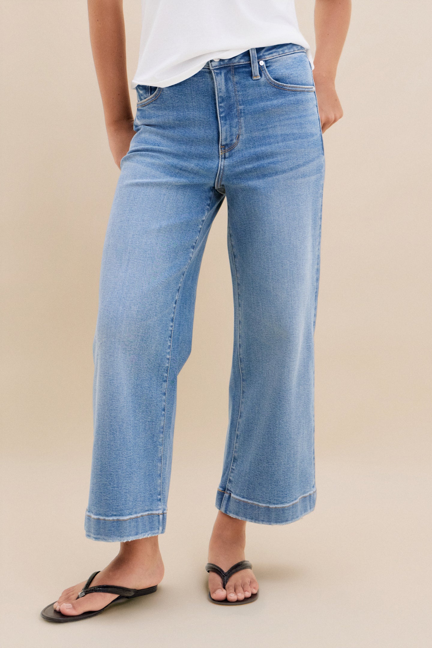 Person wearing light blue jeans on a beige background