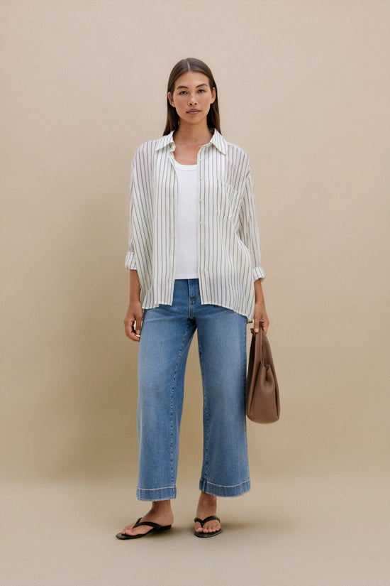 Woman wearing a striped shirt, jeans, and carrying a brown bag on a beige background